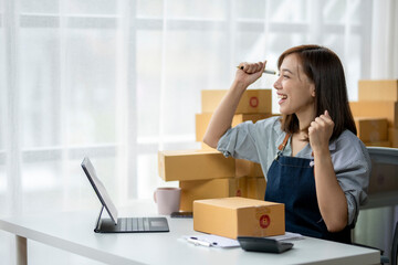 A woman is sitting at a desk with a laptop and a stack of boxes in front of her