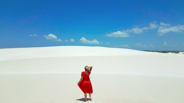 Aerial view of Lady in red dress spin around on white sand dunes in Brazil desert in Parque Nacional dos Lencois Maranhenses. Attractive young woman in red dress.