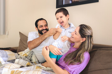 Family on the sofa at home having fun together. The father tickles his little son while the mother...