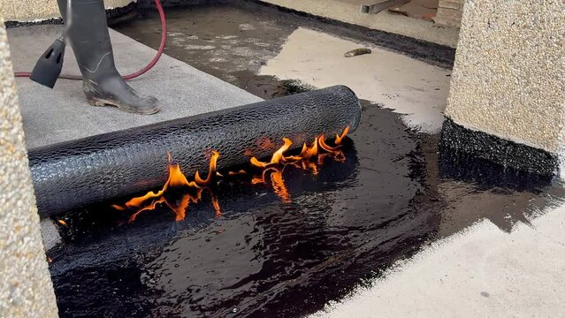 Construction worker heating with a blow torch an bituminous material and rolled across a concrete surface
