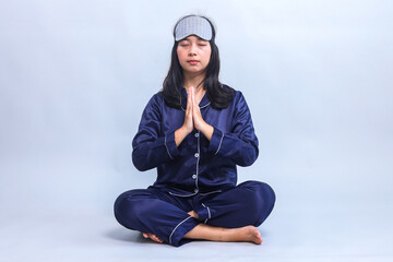 Full body of woman sitting in pajamas and sleep eye mask doing meditation before sleep