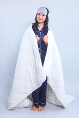 Full length of young woman in pajamas and eye mask covered with blanket isolated on white background