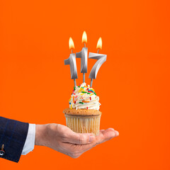 The hand that delivers cupcake with the number 117 candle - Birthday on orange background