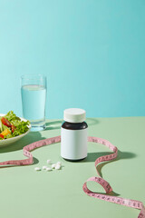 Weight losing theme photograph against blue background, a blank bottle of medicine featured in...
