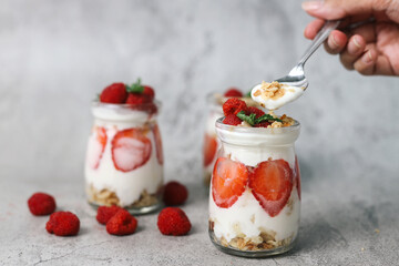 Hand Taking A Spoonful of Dessert Strawberry Parfait Over Grey Background