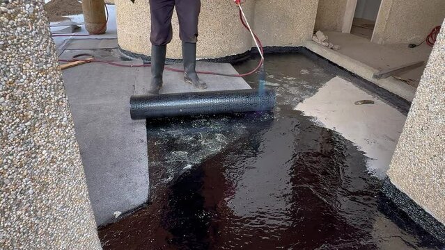 Construction worker heating with a blow torch an bituminous material and rolled across a concrete surface