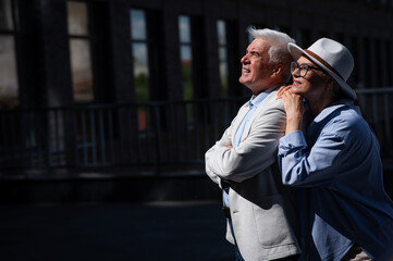 Stylish mature couple on a walk. Portrait of gray-haired man and woman hugging outdoors. 