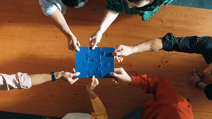 Top down view of skilled business people assemble blue jigsaw puzzle on meeting table. Group of...