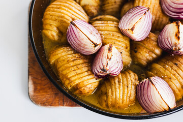 plant-based roasted hasselback potatoes with onions in round oven tray