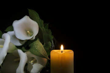 White calla lily flowers and burning wax candle in darkness