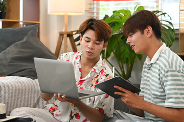 Happy young gay male couple planning vacation trip, using laptop for booking a hotel on website