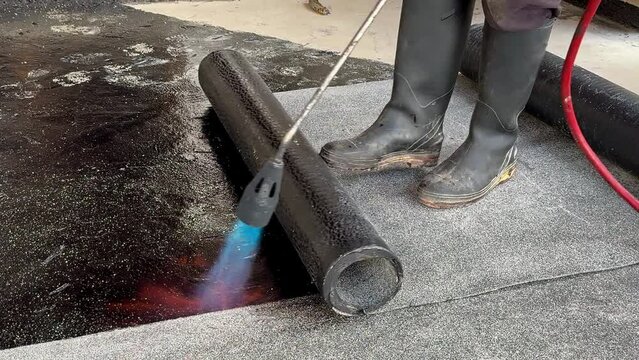 Construction worker heating with a blow torch an bituminous material and rolled across a concrete surface