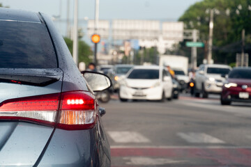 Rear side of grey car with turn on brake light. On body of car with drop of water after rainy. Traffic on the asphalt road many cars in the opposit of crossroads road.