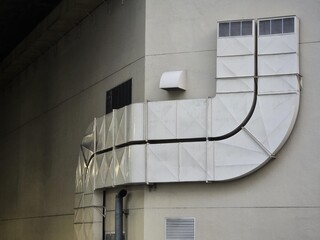 Large air duct outside the building Attached to the side of the building are 2 pipes.