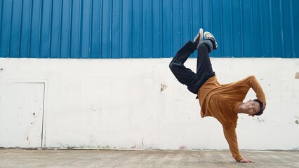Hispanic man stretch arms and dance street dancing in front of wall. Motion shot of stylish dancer...