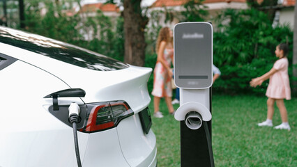 Electric vehicle recharge from home charging station on background of happy and playful family...