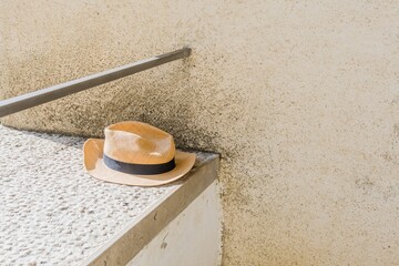 A brown hat with a black band placed on concrete ledge with a textured wall in the background, in...