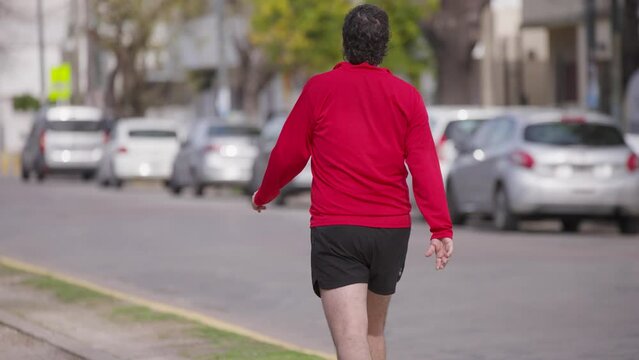 Hombre vestido de rojo de espaldas camina por el parque.