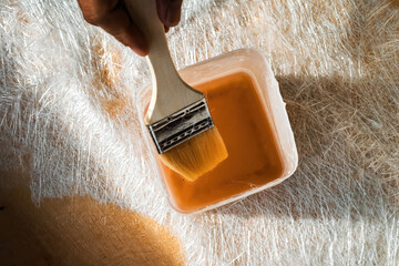 Paint brush inside the fiberglass solution in a container on top of the fiberglass sheet.