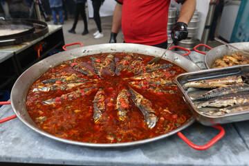 Fish is being cooked in a huge pan at an outdoor food festival.