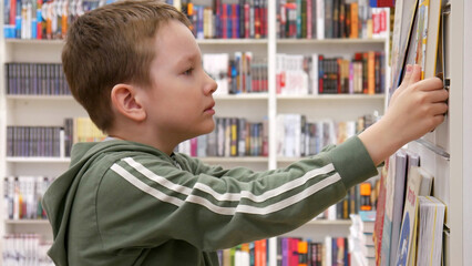 Close-up of a cute boy taking a book from the stand of a book shop or library