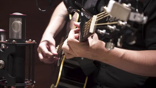 Guitarrista tocando guitarra ac&uacute;stica con transporte, en estudio de grabaci&oacute;n con una camisa negra. Footage de m&uacute;sica, musical, grabaci&oacute;n en estudio, producci&oacute;n musical.