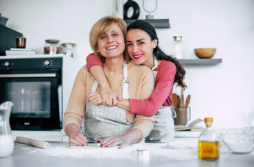 Mature happy mother and her cute daughter in aprons are cooking on kitchen. Having fun together while making pie, cakes and cookies. Working with dough together