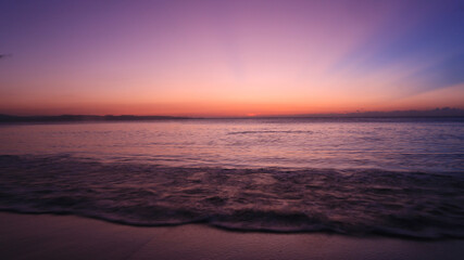 Sunset by the shore. Waves crashing into fine white sand during golden hour
