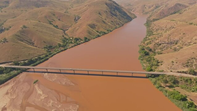 Top down view of car crossing huge bridge above Tsiribihina River in Madagascar countryside. Dirty river with yellow color after soil erosion.