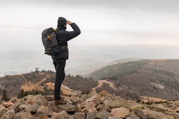 A male hiker stands on top of a rocky outcrop and looks out over the landscape shielding his eyes...