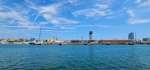 Wide angle view of shipping docks in the Mediterranean, with calm blue sea and blue sky with light clouds, construction cranes and loading and unloading equipment.