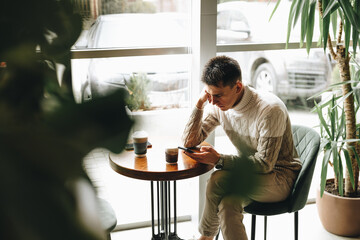Young Man Engrossed in Smartphone at a Modern Cafe During Daytime