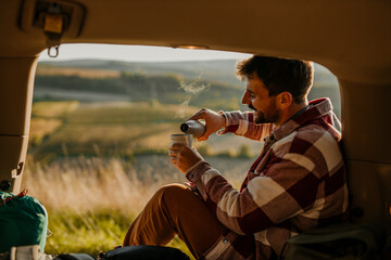 Adventurous man sitting in his truck, drinking a hot tea, ready to explore golden hills