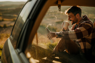 Adventurous man sitting in his truck, drinking a hot tea, ready to explore golden hills