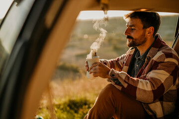 Adventurous man sitting in his truck, drinking a hot tea, ready to explore golden hills