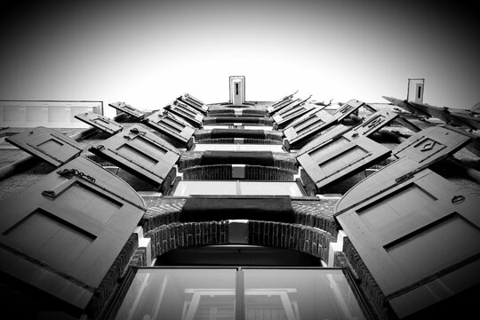 L'immagine mostra una foto in bianco e nero di un edificio ad Amsterdam. L'edificio &egrave; a tre piani ed &egrave; caratterizzato da una facciata simmetrica con numerose finestre e persiane. Le finestre sono rett