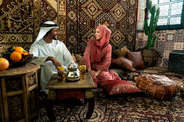 Young couple from Emirati spending time in an arabian traditional cafe. Man and woman wearing...