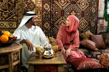 Young couple from Emirati spending time in an arabian traditional cafe. Man and woman wearing...
