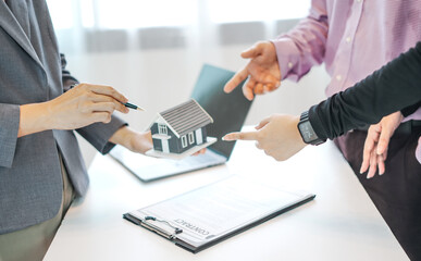 An official's hand points to a house model and explains details, contracts, and insurance to the couple who come to buy the house
