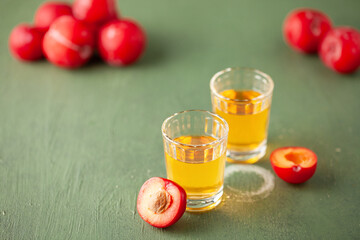 Plum brandy or plum vodka, strong drink in glasses on  table. Balkan Slivovica. Fresh red plums. Copy space