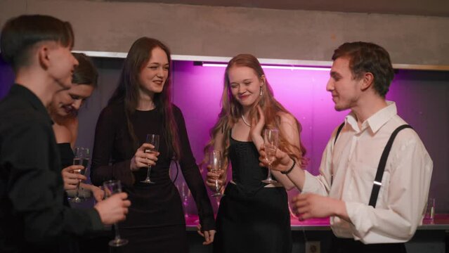 Group of young people enjoy dancing. Cheerful company dancing holding glasses of champagne for cocktails drinking alcoholic beverages have fun in night club. Nightlife, birthday party concept.