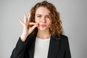 Young Woman Gesturing Silence With Finger on Lips Against a Grey Background