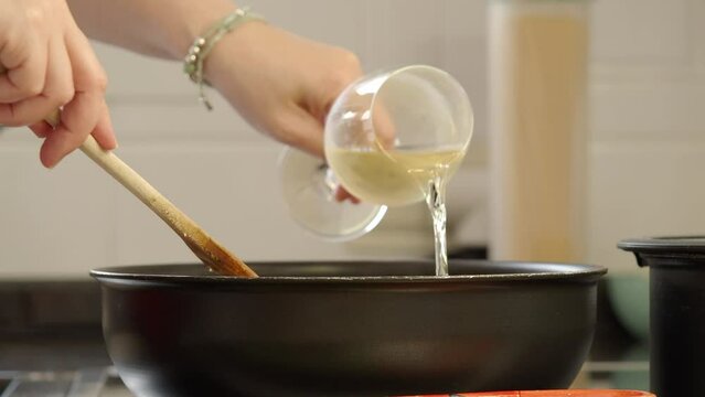 Adding white wine to a sauce boiling in a pan.