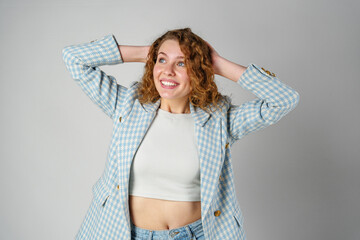 Young woman with curly hair in blue jacket posing on gray background