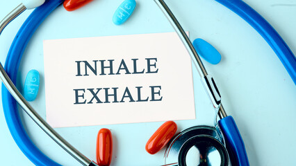 INHALE EXHALE written words on a white business card on a blue background with a stethoscope, pills...