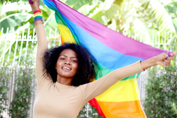 Happy smiling homosexual lesbian African woman with curly hair holding rainbow flag. Beautiful girl celebrating pride month outdoor. Cheerful LGBT and gay pride celebration movement concept.