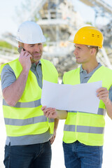 two men wearing reflective clothing looking at plans on site