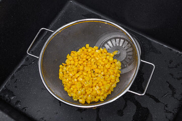 Odsączać kukurydzę konserwową z zalewy na sitku w zlewie