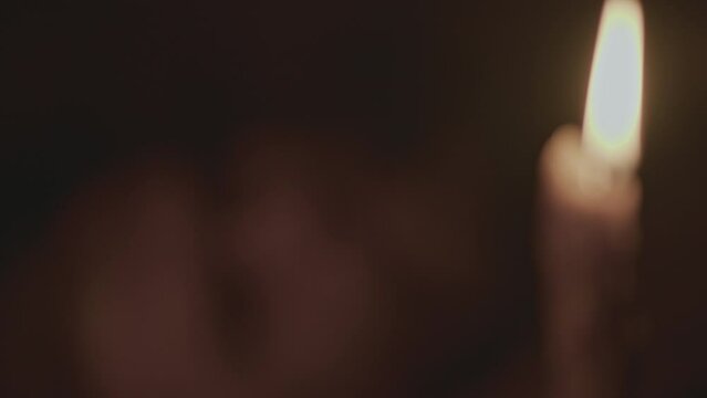 Close up of burning candle and a male face behind in a dark room. Media. Ancient house lighting and a lying man at night.