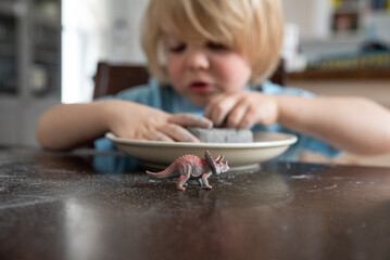 Child digging dinosaur toy out of clay at kitchen table